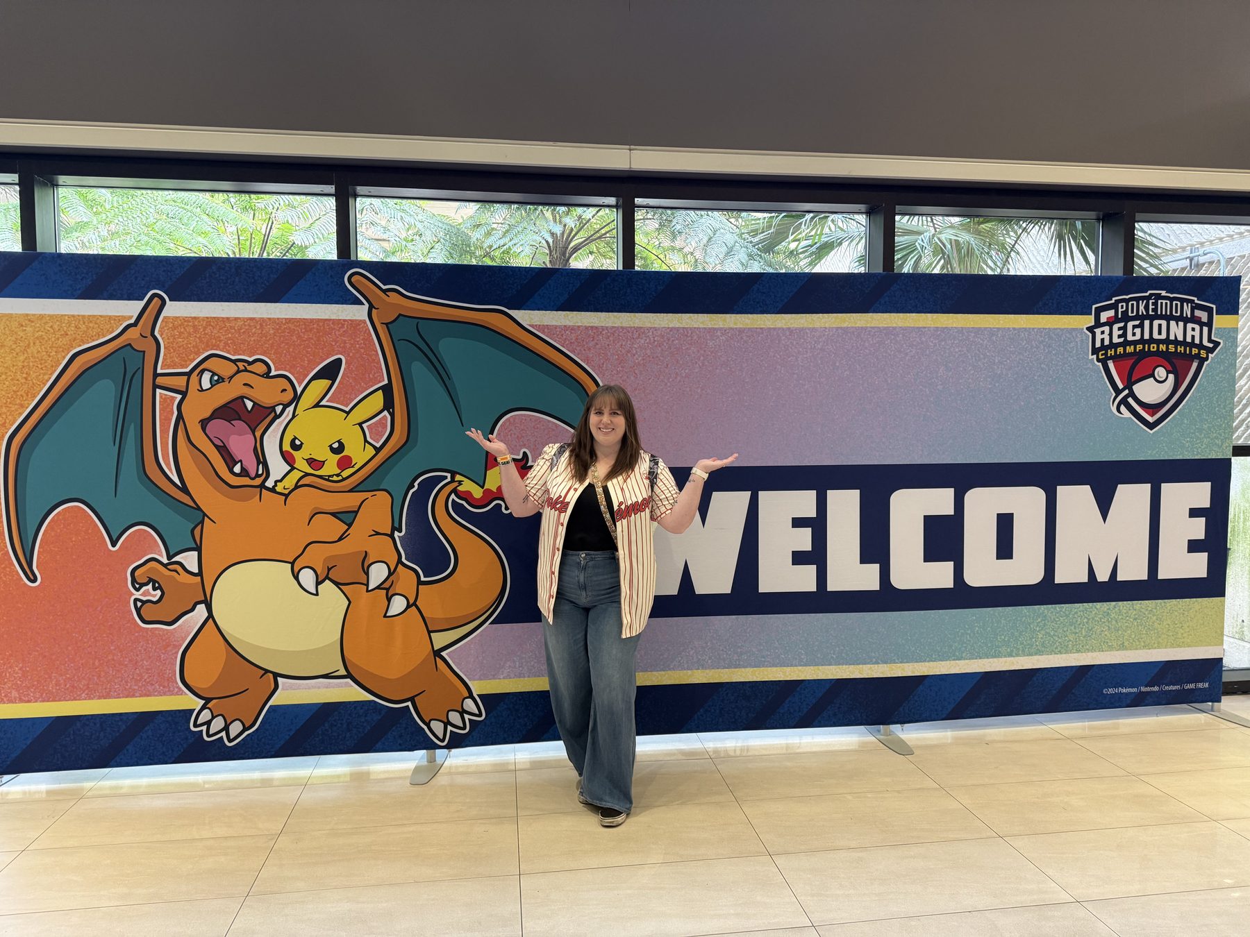 Bry at an official Pokémon Regional Championships, standing in front of a welcome banner with Charizard and Pikachu