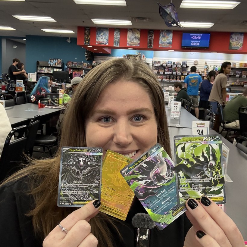 Bry holding Mega Darkrai ex Pokémon cards at a card shop